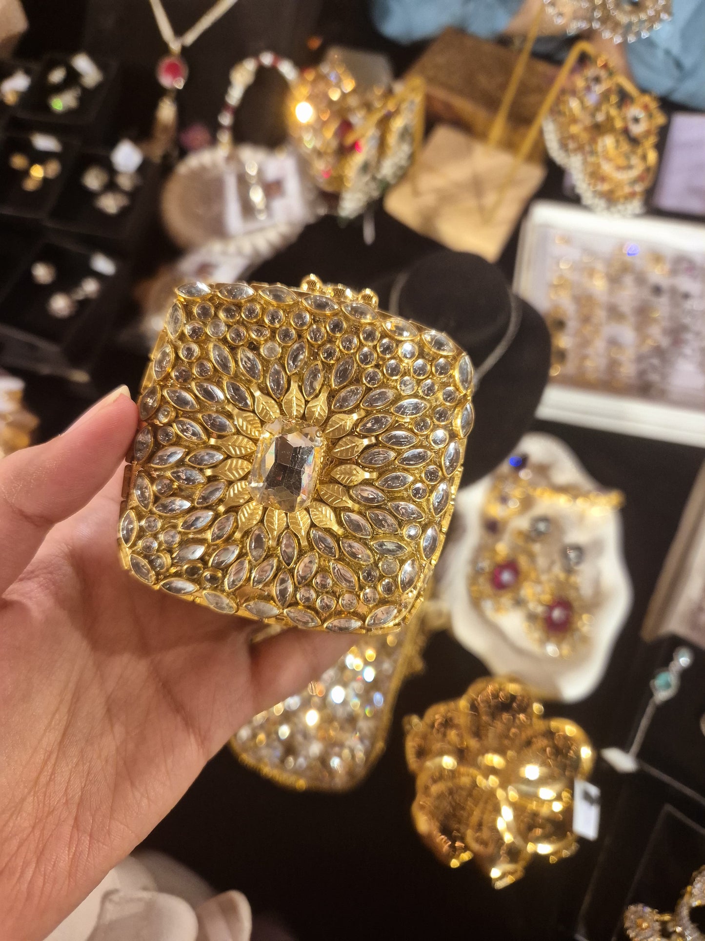 Gold-toned Kundan Polki hand clutch with marquise stone detailing held in hand