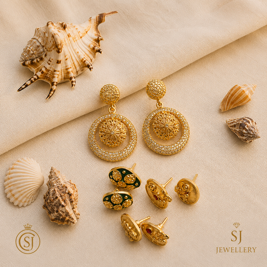 Gold filigree round statement earrings with crystal pavé, alongside three gold stud earring pairs with enamel and stone detailing, displayed on cream fabric with seashells