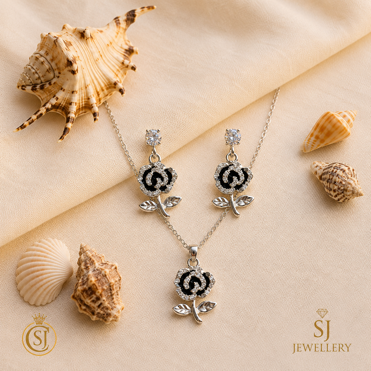 Silver-tone black rose pendant necklace and matching drop earrings with crystal stone detailing, displayed on cream fabric with seashells