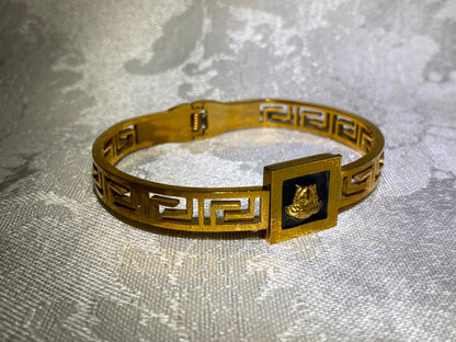 Handcrafted gold-tone bangle cuff with Greek key motif and engraved emblem plaque