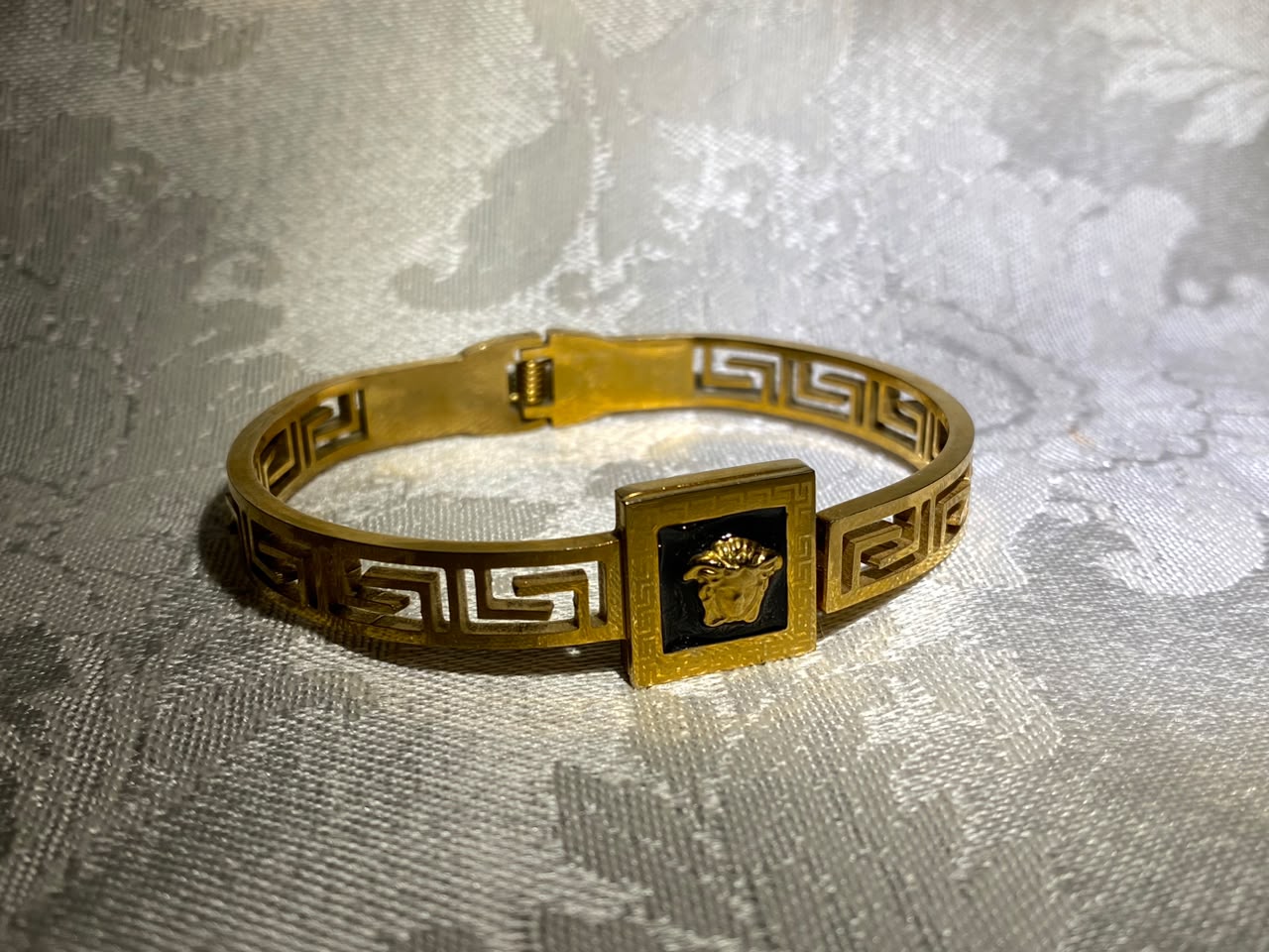 Handcrafted gold-tone bangle cuff with Greek key motif and engraved emblem plaque